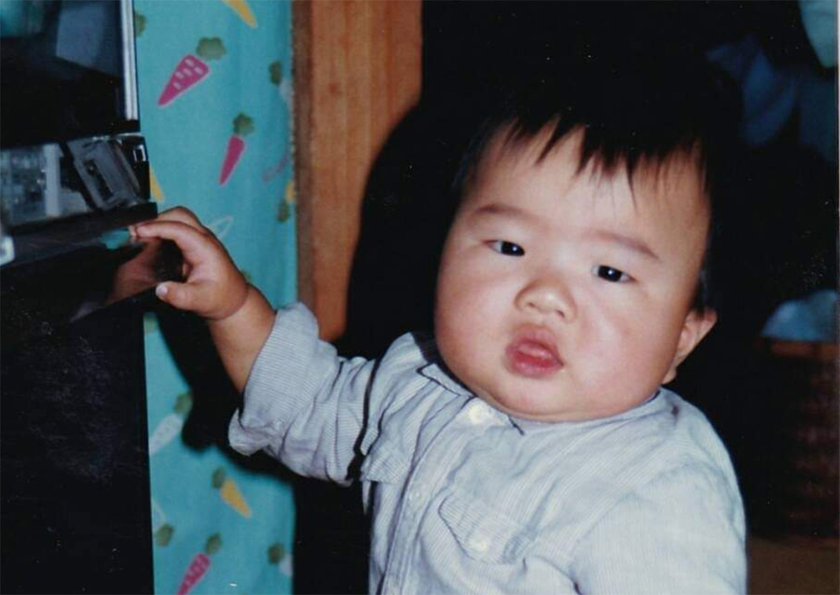 原田メガホンが２歳の頃の写真の画像。水色のシャツを着てボーッとカメラを見ている様子